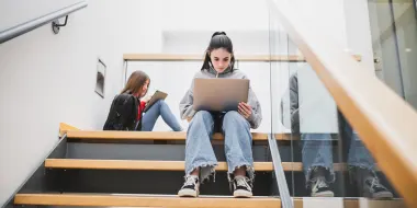 Female students use laptops in stairwell. (© istock.com/iantfoto